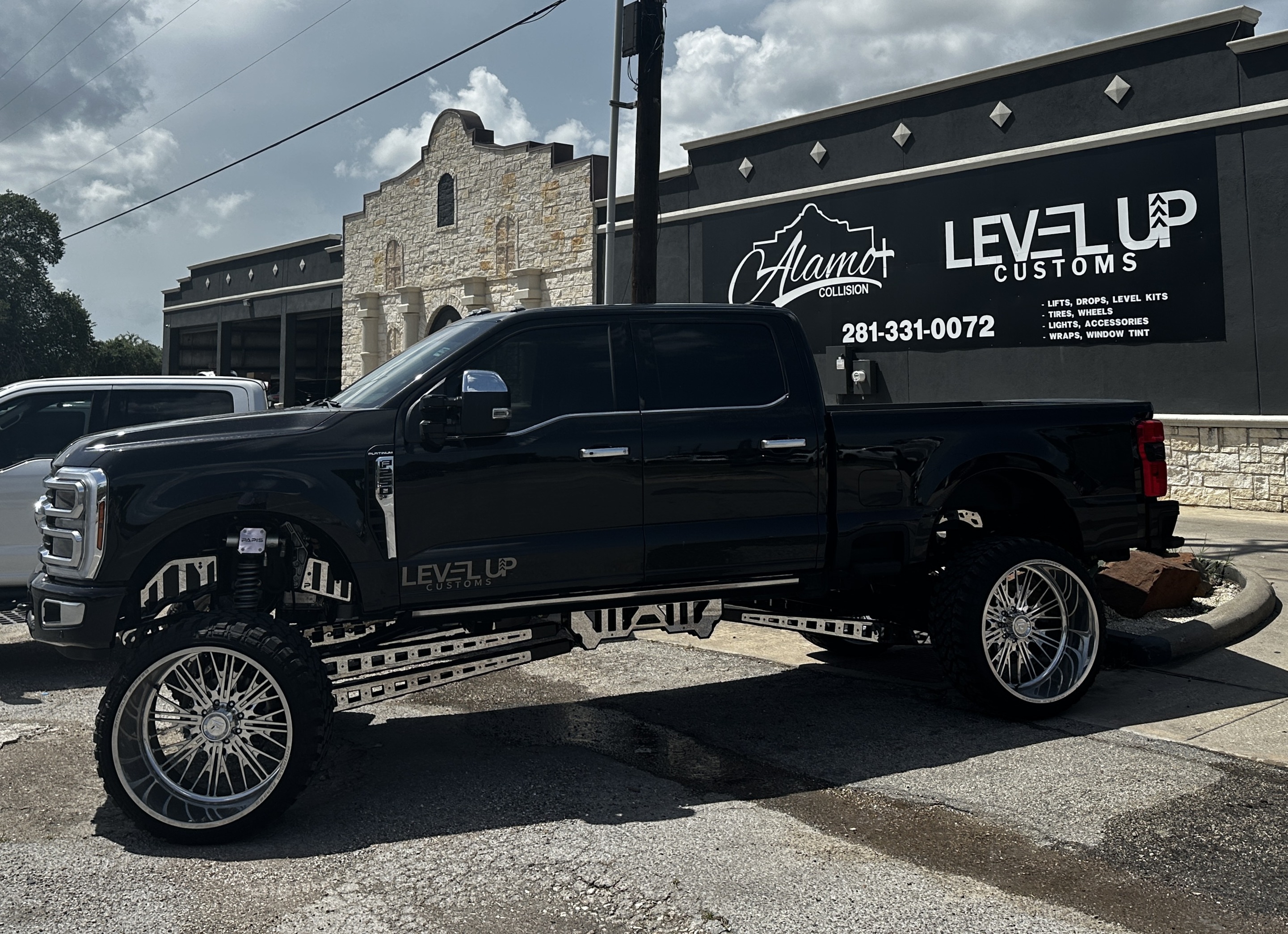 Alamo Collision and Level Up Customs shop &mdash; lifted black Ford F-250 Platinum in front of Alvin TX location